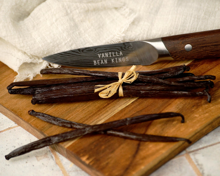 Vanilla beans on a wooden cutting board with a knife labeled 'Vanilla Bean Kings'.