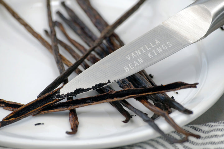 Vanilla bean pods with a knife on a white plate