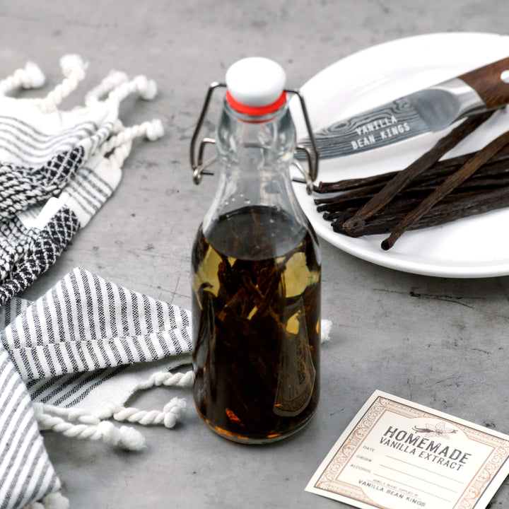 Bottle of homemade vanilla extract on a gray surface with vanilla beans and a label.