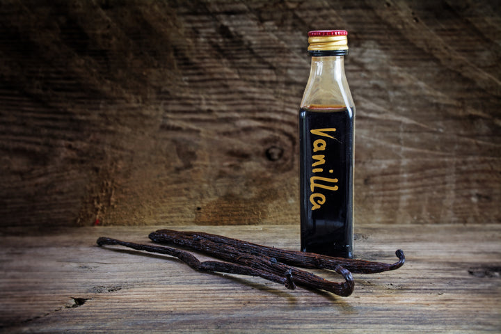 3 vanilla beans on table with bottle of vanilla extract